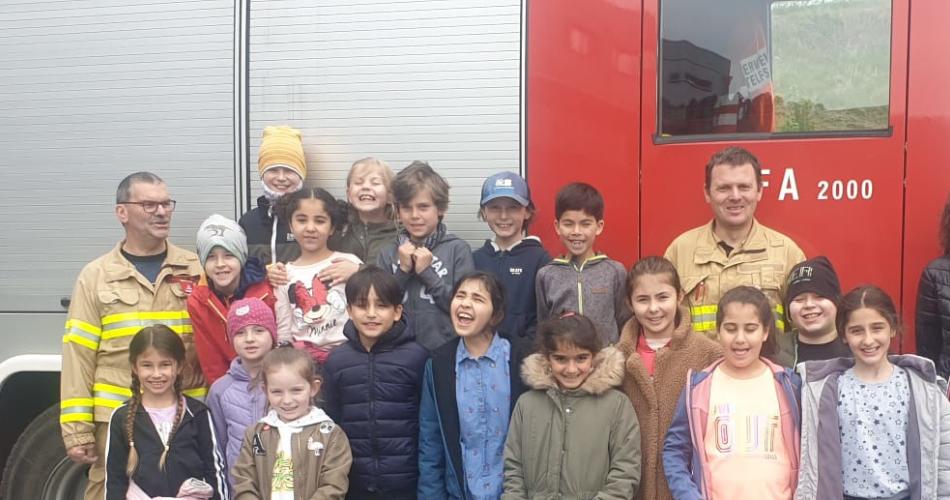 Klassenfoto mit Feuerwehrmännern und Feuerwehrauto im Hintergrund