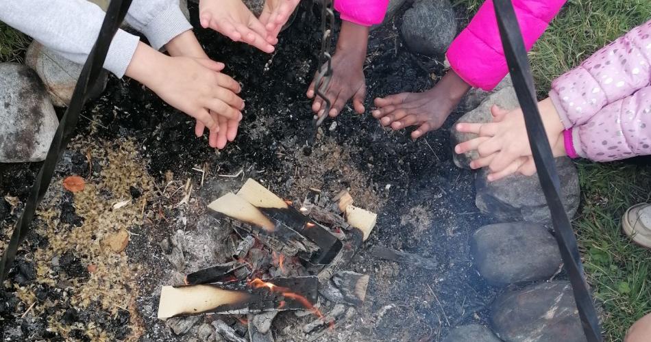 Kinder wärmen sich am Lagerfeuer die Hände