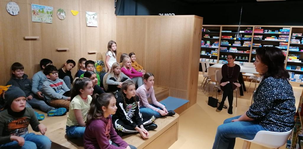 Kinder sitzen auf der Bühne, Bibliothekarin liest ein Buch vor