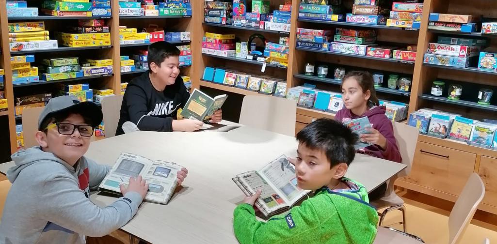 Kinder sitzen beim Tisch in der Bücherei und lesen Bücher