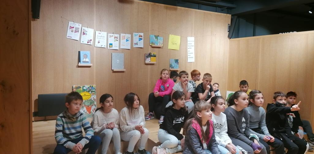 Kinder sitzen auf der Bühne und hören zu