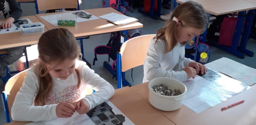 Kinder legen den Buchstaben mit Steinen nach