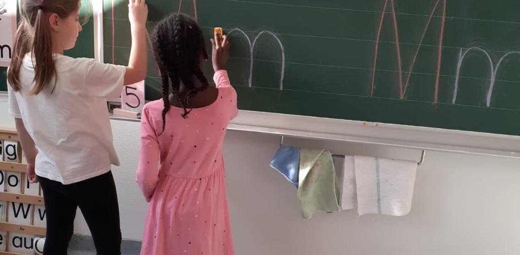 Kinder fahren den Buchstaben an der Tafel nach