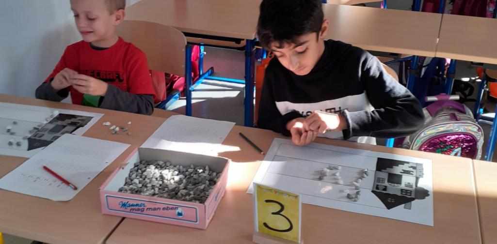 Kinder legen den Buchstaben mit Muggelsteinen nach