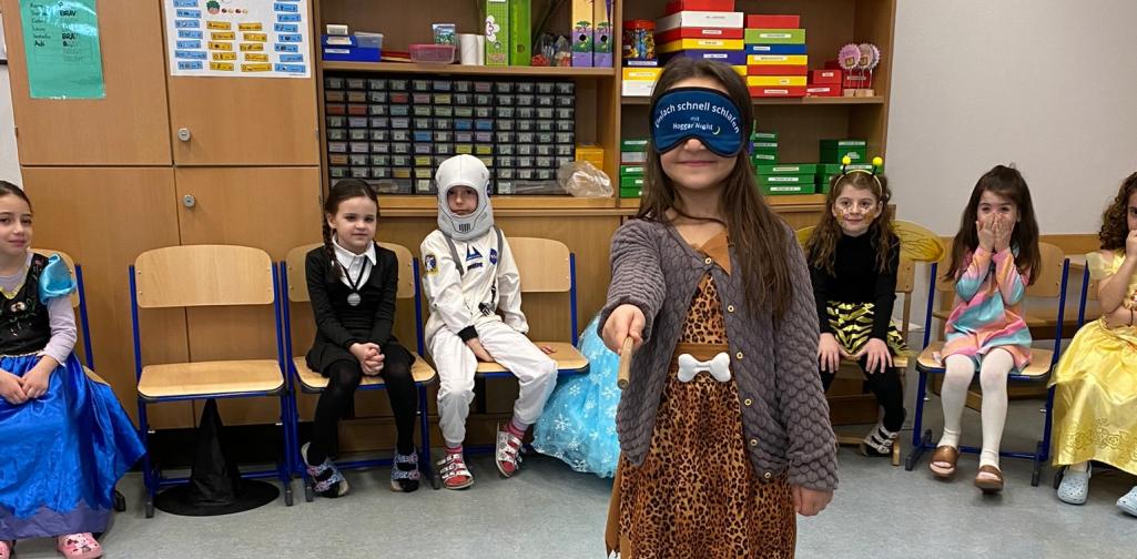 Fasching 4 Kinder sitzen im Sitzkreis, ein Kind steht mit verbunden Augen in der Mitte