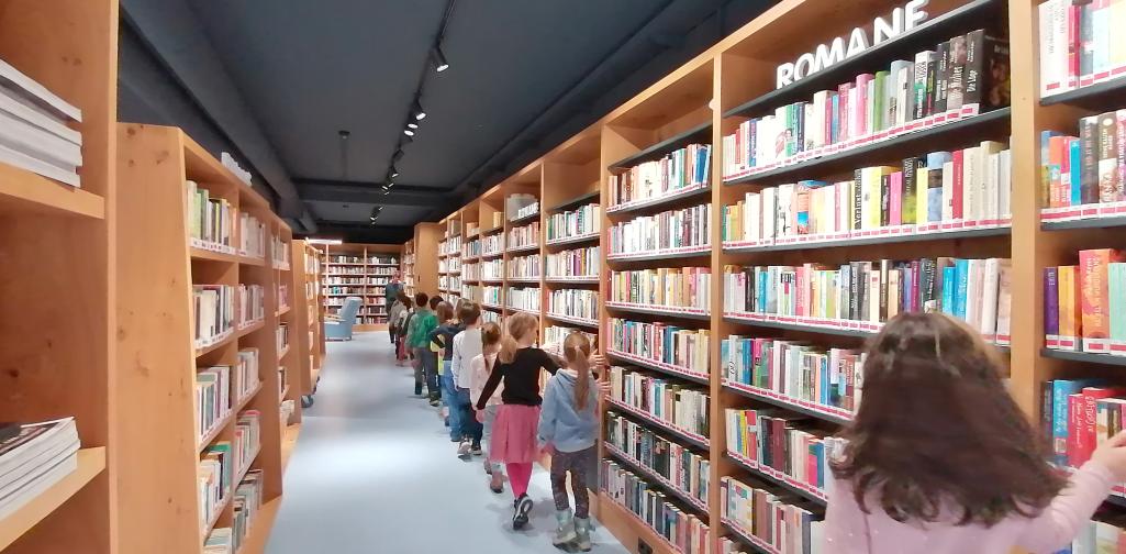 Bücherei 1 Kinder streichen über die Buchrücken der Bücher in den Regalen