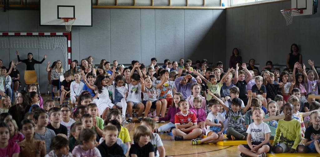 Abschlussfeier 12 Kinder aller Klassen sitzen im Turnsaal