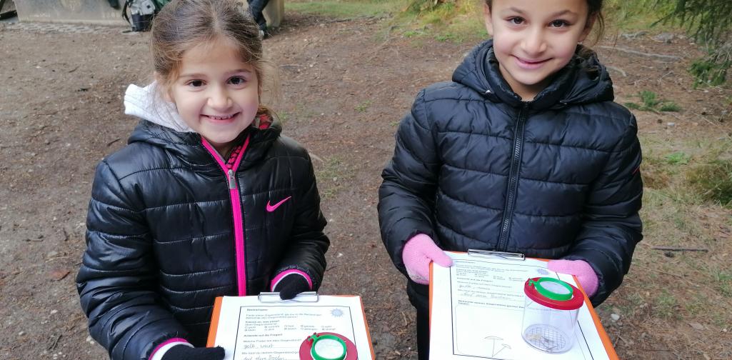 Wald 1 Kinder zeigen Klemmbrett und Becherlupe