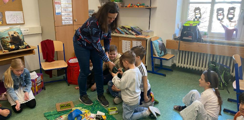 Die Expertin zeigt den Kindern eine Glasflasche mit einem Fehler
