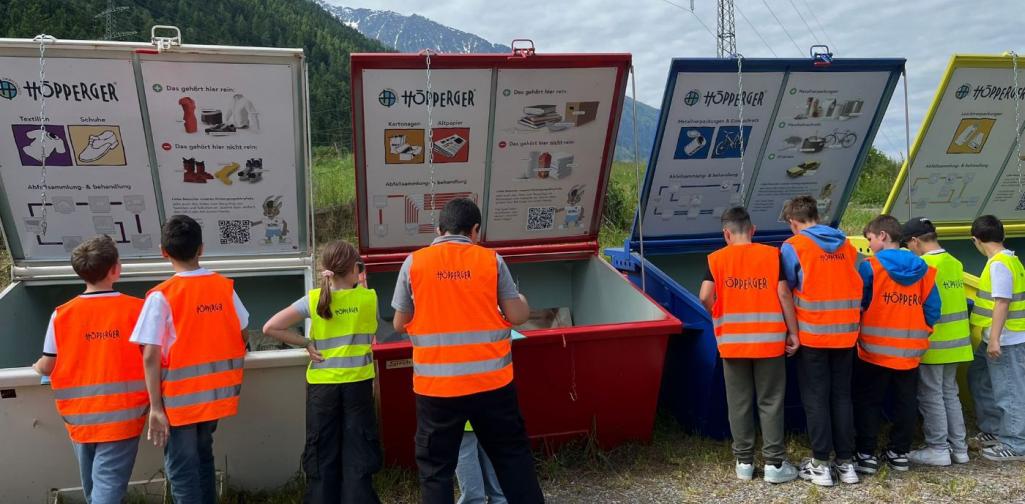 Kinder stehen vor verschieden farbigen Containern