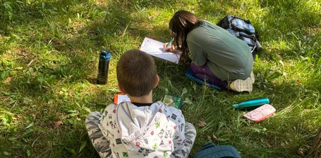 Kinder sitzen im Gras und lösen ihre Aufgaben