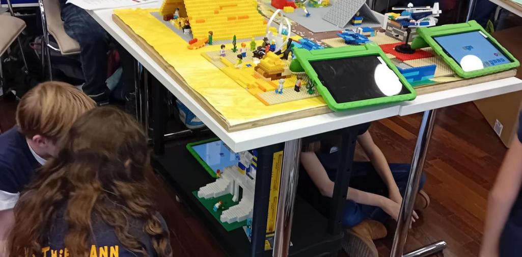 Modell aus Klemmbausteinen, stellt eine Pyramide dar, Tabletts liegen am Tisch, Kinder sitzen unter dem Tisch und betrachten das Modell einer nachgebauten Sphinx